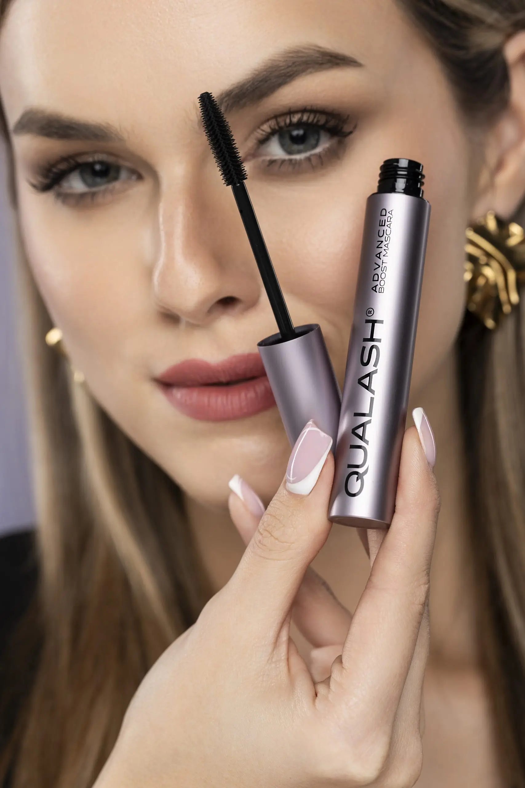 Close-up of woman holding QUALASH Advanced Volume Max with visible curved brush and voluminous lashes
