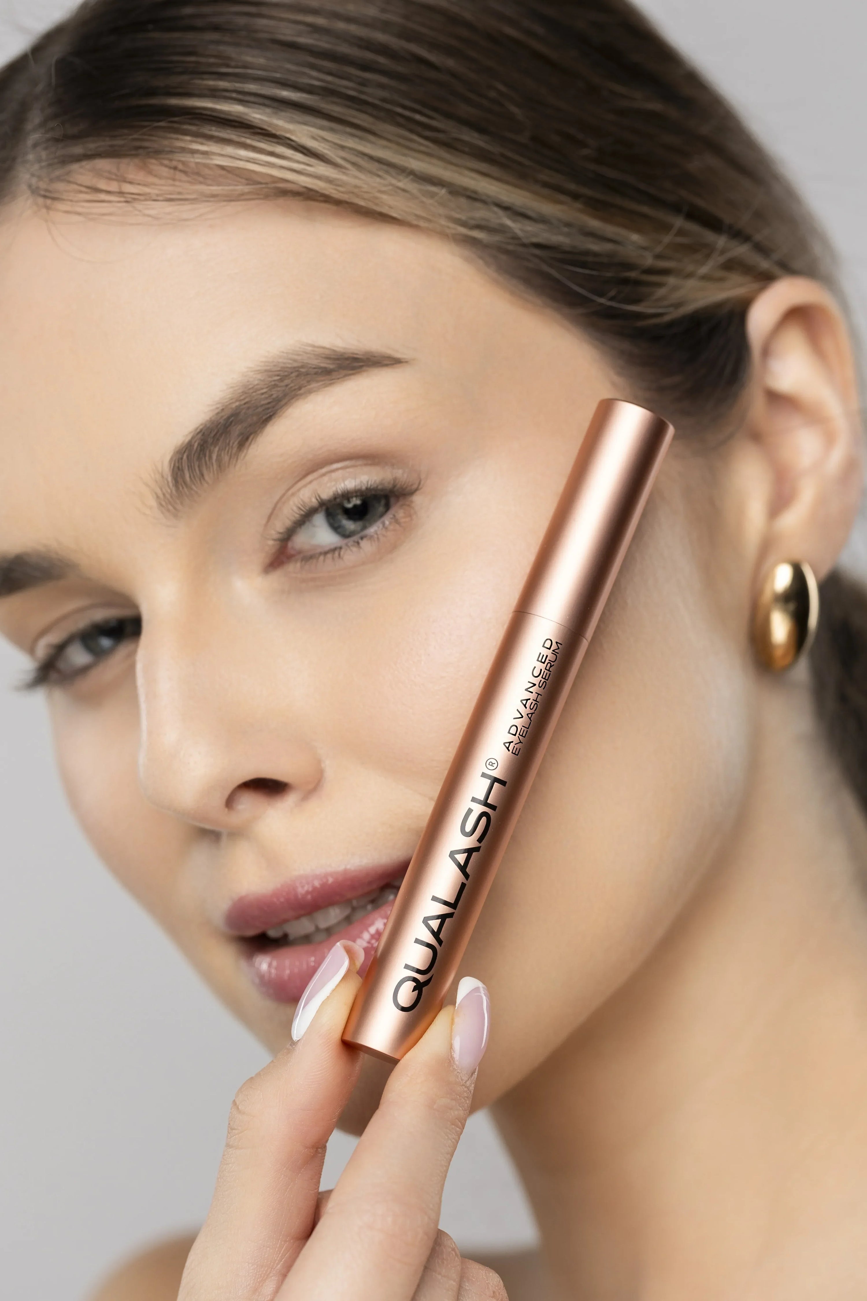 Close-up of woman holding QUALASH® Eyelash Serum next to lashes